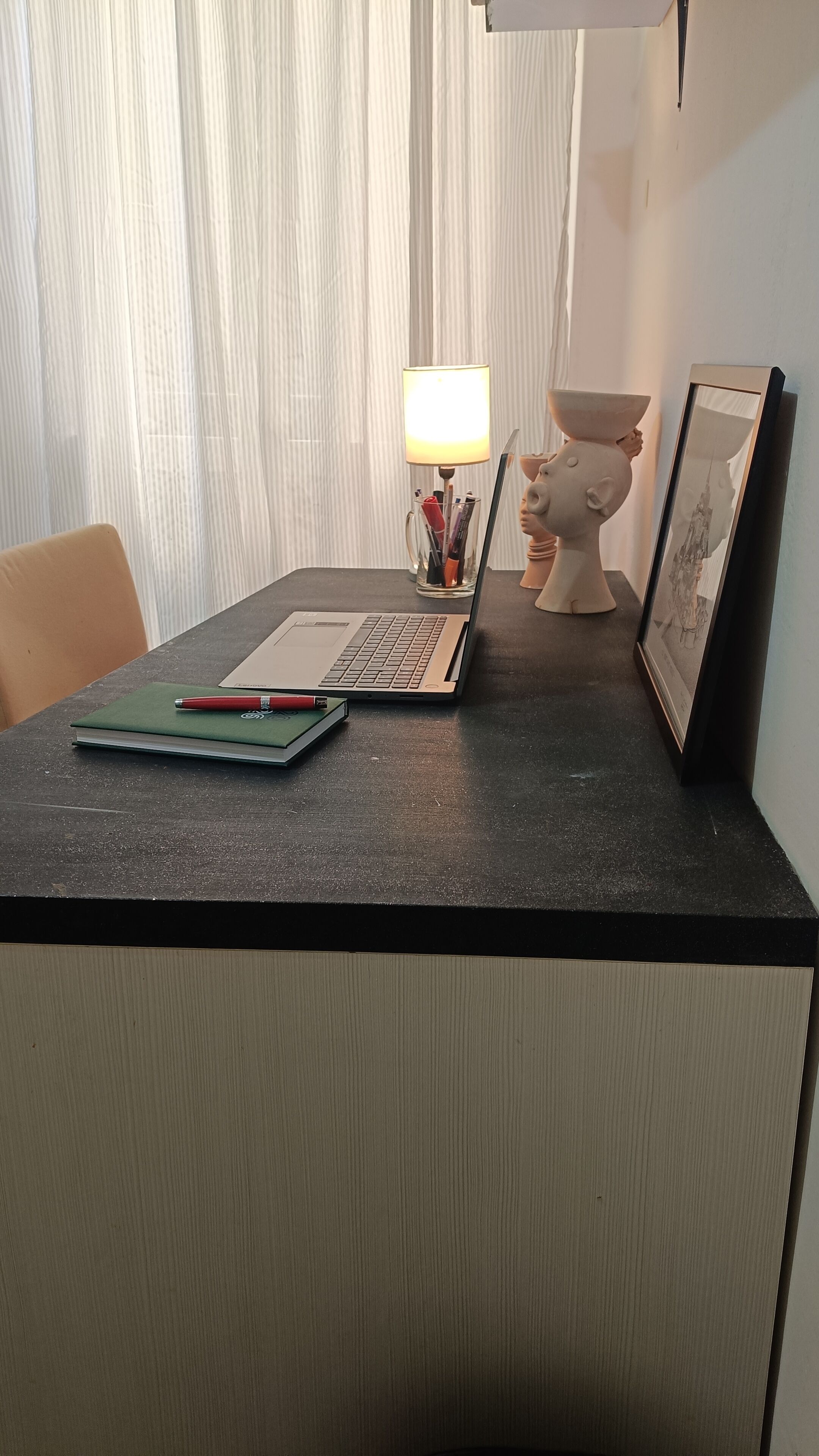 Ein Schreibtisch mit einem Laptop, einem Notizbuch, einem Stift, einer Lampe und einer dekorativen Schwein-Figur.
