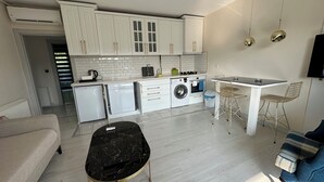 A compact kitchen with white cabinets, a washing machine, a compact fridge, and a small dining area with a table and two chairs. - Golden Hour Apartment (Bursa)
