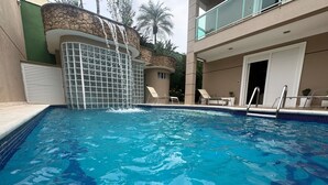 Ein Swimmingpool mit Wasserfall, umgeben von Liegestühlen und einem Gebäude mit Balkon.
