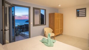 Une chambre dotée d’un grand lit, d’une chaise, d’une armoire et d’un balcon offrant une vue sur la mer.