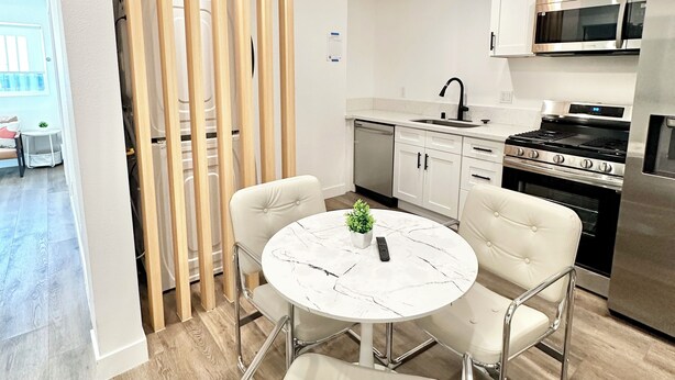 Una cucina moderna con mobili bianchi, elettrodomestici in acciaio inossidabile e un tavolo tondo in marmo con quattro sedie.