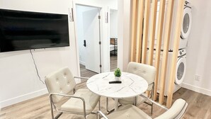 Un soggiorno moderno con un tavolo rotondo in marmo, quattro poltrone imbottite, una TV a schermo piatto montata a parete e un divisorio in listelli di legno.