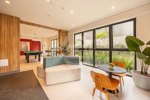 A modern living room with a pool table, a sofa, a dining table with chairs, and large windows. - Estúdio Premium Vila Olímpia -ap1901 (Sao Paulo)