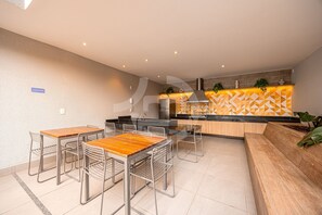 A modern kitchen with a dining area, featuring a wooden table, metal chairs, and a built-in bench. - Estúdio Premium Vila Olímpia -ap1901 (Sao Paulo)