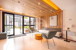 A modern hotel lobby with a wooden ceiling, a reception desk, a seating area with a sofa and chairs, and a large window offering a view of the outdoors. - Estúdio Premium Vila Olímpia -ap1901 (Sao Paulo)