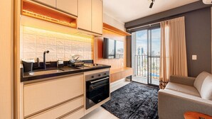 A modern kitchen with a built-in oven, a large window with a view of the city, and a flat-screen TV mounted above the counter. - Estúdio Premium Vila Olímpia -ap1901 (Sao Paulo)