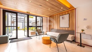 A modern hotel lobby with a wooden ceiling, a reception desk, a seating area with a sofa and chairs, and a large window offering a view of the outdoors. - Estúdio Premium Vila Olímpia -ap1901 (Sao Paulo)