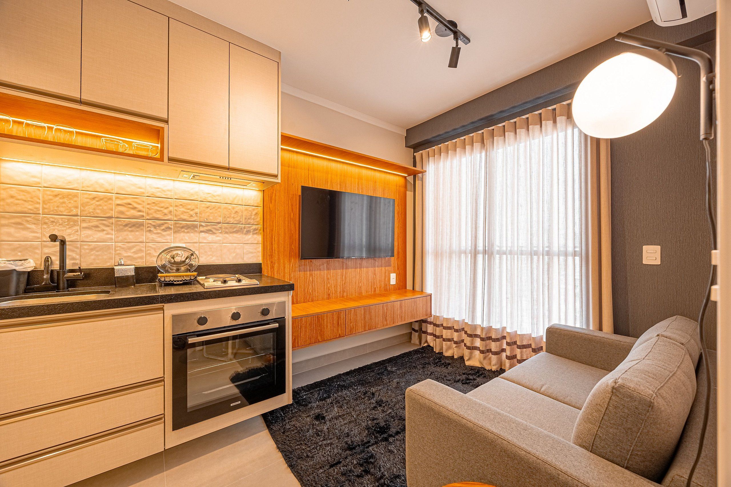 A modern kitchen with built-in appliances, a flat-screen TV, and a cozy seating area with a large window.