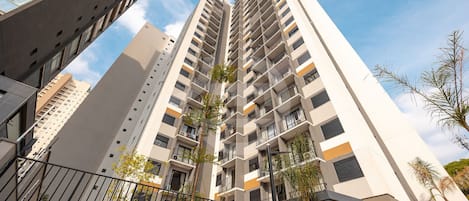 Un edificio residenziale di grattacielo con numerosi balconi, un ingresso carrabile e vegetazione circostante.