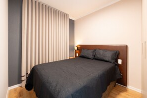 A bedroom with a bed, curtains, a nightstand, and a wall-mounted lamp. - Estúdio Premium Vila Olímpia -ap1901 (Sao Paulo)