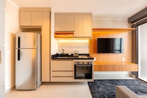 A compact kitchen with a built-in oven, a refrigerator, and a flat-screen TV mounted on the wall. - Estúdio Premium Vila Olímpia -ap1901 (Sao Paulo)
