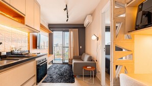 A modern kitchen with a built-in oven, a dining area with a small table, and a living space with a sofa and a TV. - Estúdio Premium Vila Olímpia -ap1901 (Sao Paulo)