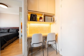 A compact room with a bed, a kitchenette with a coffee maker, microwave, and a phone, and two chairs. - Estúdio Premium Vila Olímpia -ap1901 (Sao Paulo)