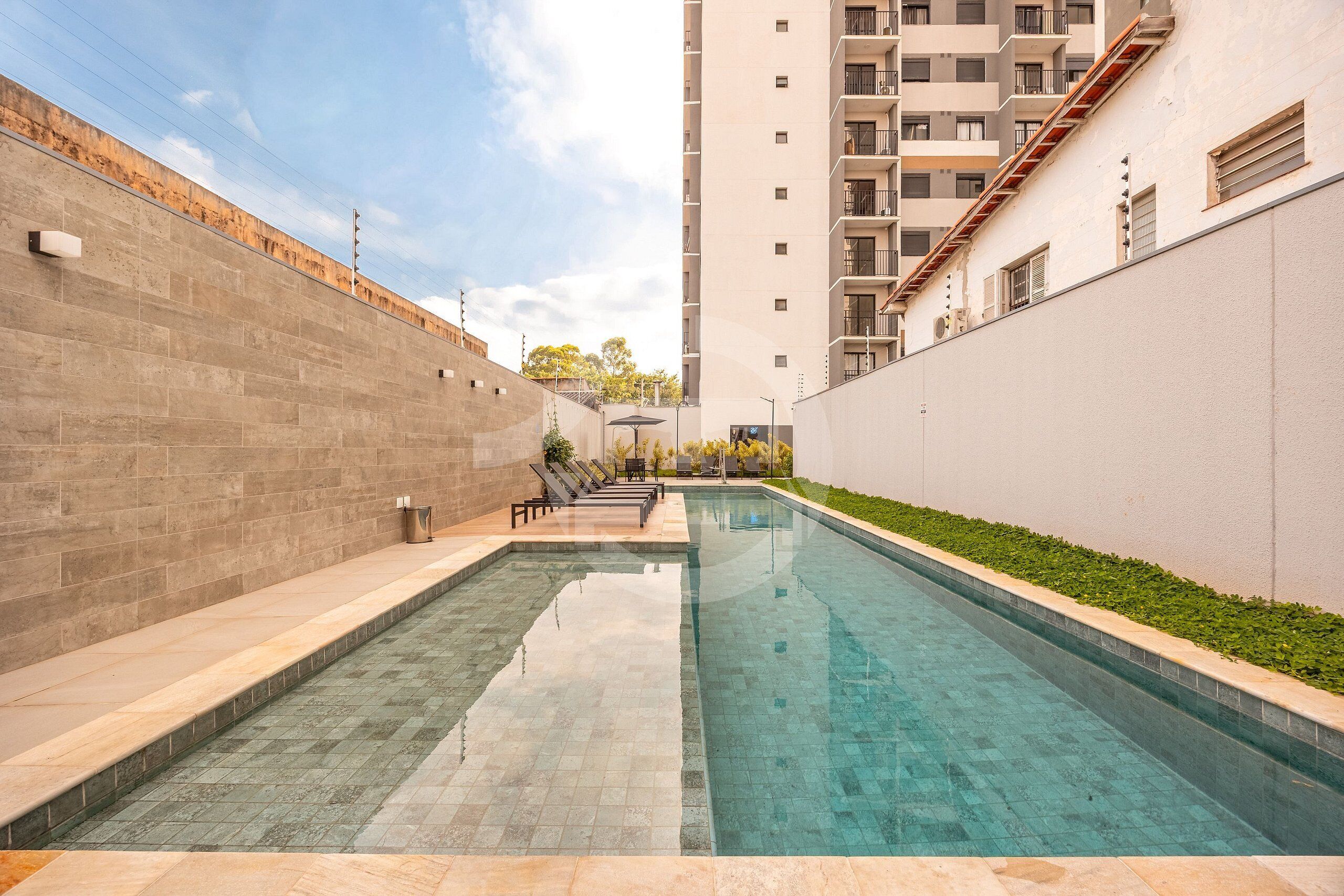 A swimming pool with a tiled deck, surrounded by a high-rise building with balconies.