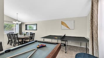Een pooltafel met biljartballen, een tafeltennistafel en een eethoek met stoelen en een tafel.