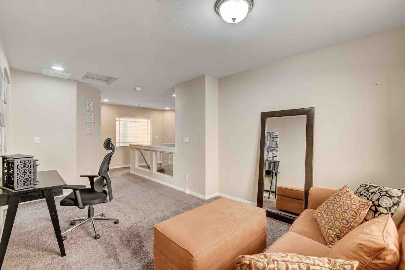 Ein Wohnzimmer mit einem braunen Sofa, einem schwarzen Bürostuhl, einem Schreibtisch und einem großen Spiegel.