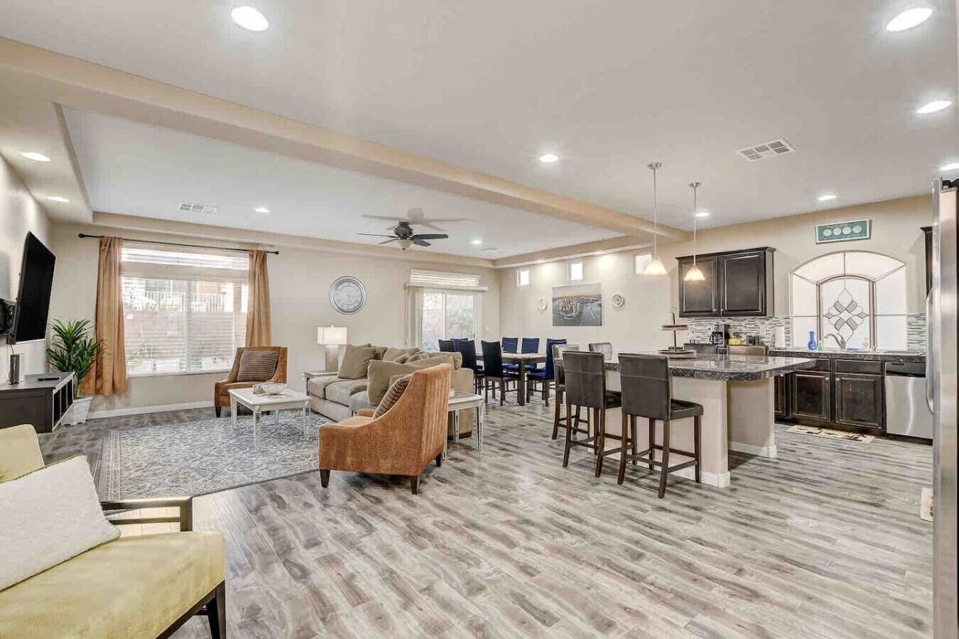 A spacious living area with a large sofa, a coffee table, and a dining table with chairs. There is a kitchen area with a refrigerator, stove, and sink.