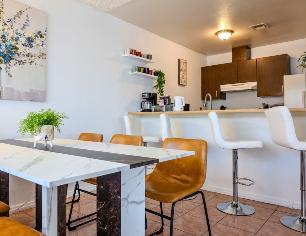 Een moderne keuken met witte kasten, een marmeren aanrechtblad en een bar met witte krukken.