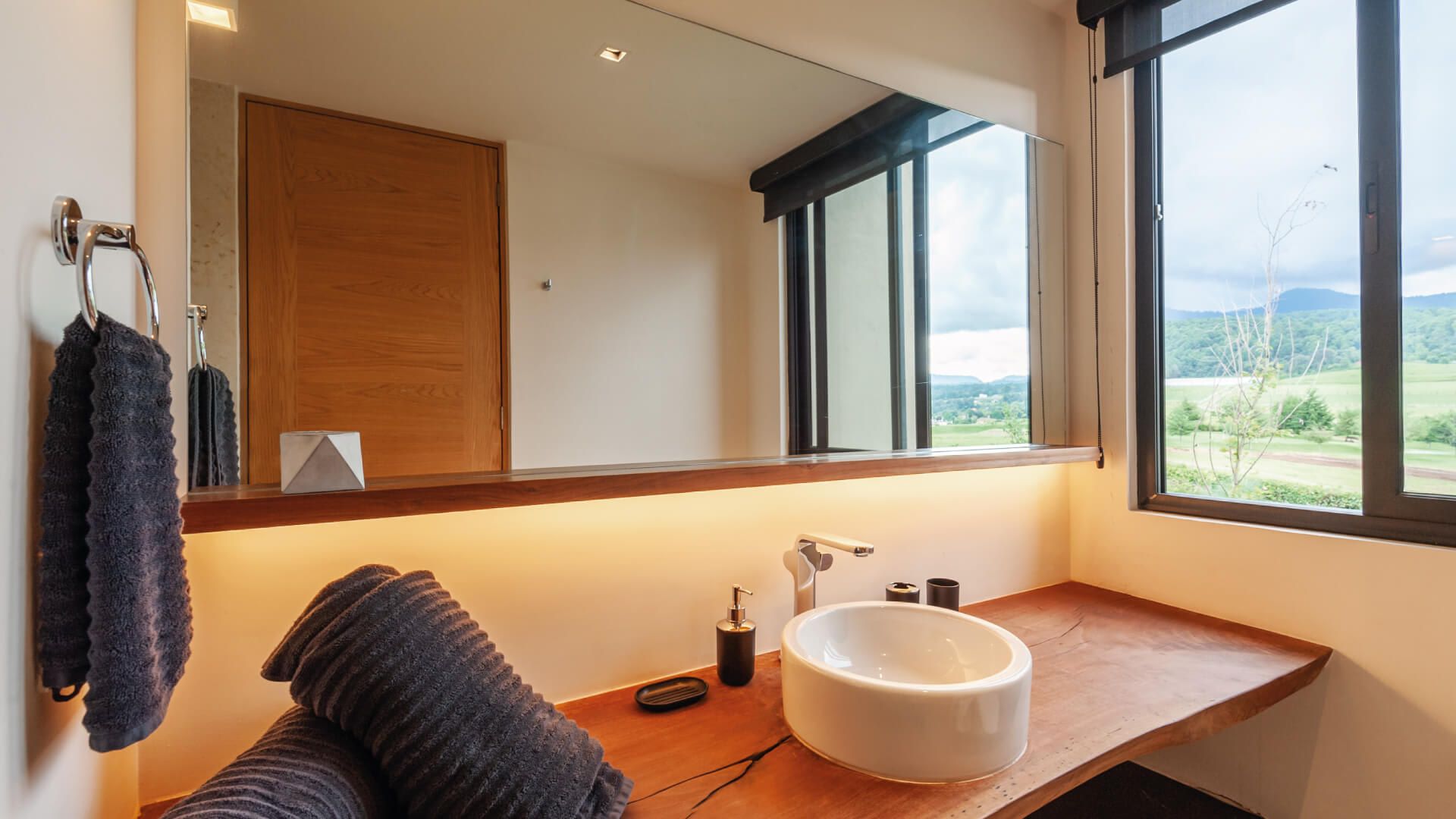 A bathroom with a wooden vanity, a large mirror, and a view of the outdoors.