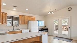 Una cocina con armarios de madera, una isla grande con taburetes, un refrigerador, un lavavajillas y un televisor.