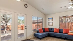 Una sala de estar con un sofá modular, un ventilador de techo y vistas al patio trasero a través de amplios ventanales.
