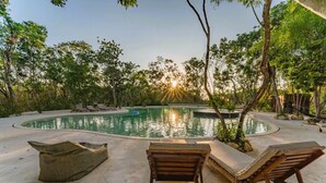 A pool area with lounge chairs and a stone bench, surrounded by trees and a clear sky. - ANANA Yaaxlum 106 S (Tulum)