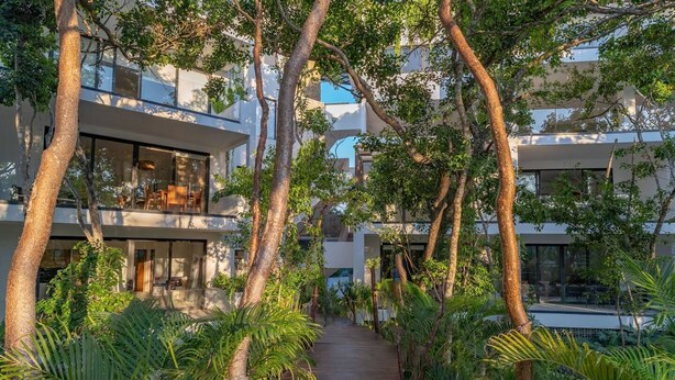 A modern building with multiple balconies, surrounded by lush greenery and trees. - ANANA Yaaxlum 106 S (Tulum)