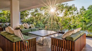 An outdoor seating area with green cushioned sofas and a central table, surrounded by a wooden fence and lush greenery. - ANANA Yaaxlum 106 S (Tulum)