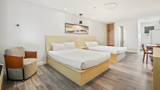 A hotel room with two beds, a chair, a desk, and a painting on the wall.