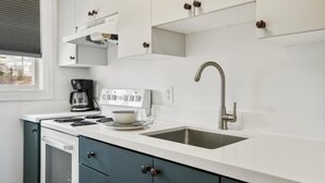 A modern kitchen with white cabinets, a stainless steel sink, a coffee maker, and a stove.