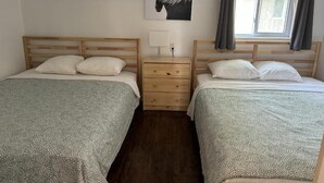 Habitación doble con dos camas, una mesita de noche, una lámpara y una ventana con cortinas.