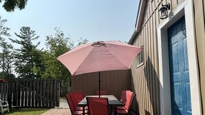 Un patio al aire libre con una mesa, sillas, un paraguas rosa y una cerca de madera.