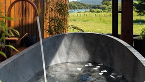 Una bañera de piedra con agua y pétalos de rosa, una pared de madera y vistas a un lago y colinas.