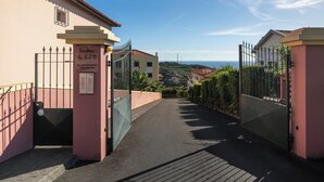 Uma entrada com portão para um terreno chamado 'Jardins do Sol II', com um caminho pavimentado que leva ao portão.