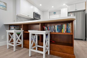 A kitchen with white cabinets, a microwave, a bookshelf with books, and a refrigerator. - Steps to the Sand@HOT TUB@Lazy Daze (Fort Myers Beach)
