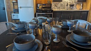 A dining table set with bowls, glasses, and cutlery in a kitchen with wooden walls, a refrigerator, and a tiled backsplash. - Owl's Nest at Feather Nest Inn (Grand Marais)