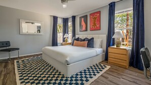 A modern bedroom with a large bed, a ceiling fan, a nightstand with a lamp, and artwork on the wall. - Playtime Bonanza House - Game Room & Playground (Austin)