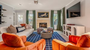A modern living room with a fireplace, orange and white furniture, and a blue patterned rug. - Playtime Bonanza House - Game Room & Playground (Austin)