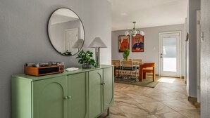 A room with a green cabinet, a round mirror, a table with chairs, and a door leading to another room. - Playtime Bonanza House - Game Room & Playground (Austin)