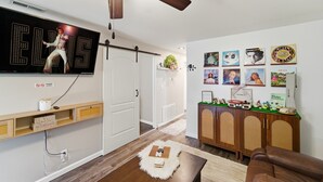 Un salon doté d’un téléviseur à écran plat, d’un meuble en bois orné d’objets décoratifs, d’un canapé en cuir marron et d’un mur décoré de tableaux encadrés.
