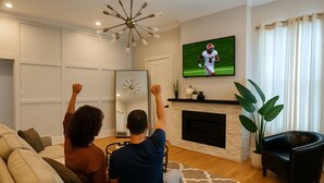 Un salon avec une cheminée, un téléviseur diffusant un match de sport et un grand miroir.