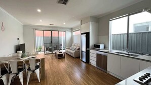 Un appartement moderne comprenant une cuisine, un coin repas et un salon. Il est doté d’une grande porte-fenêtre coulissante donnant sur un balcon, d’un téléviseur à écran plat et d’une table à manger avec des chaises.