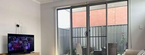 Un soggiorno con televisione, una porta scorrevole in vetro che dà su un balcone e una poltrona in vimini.