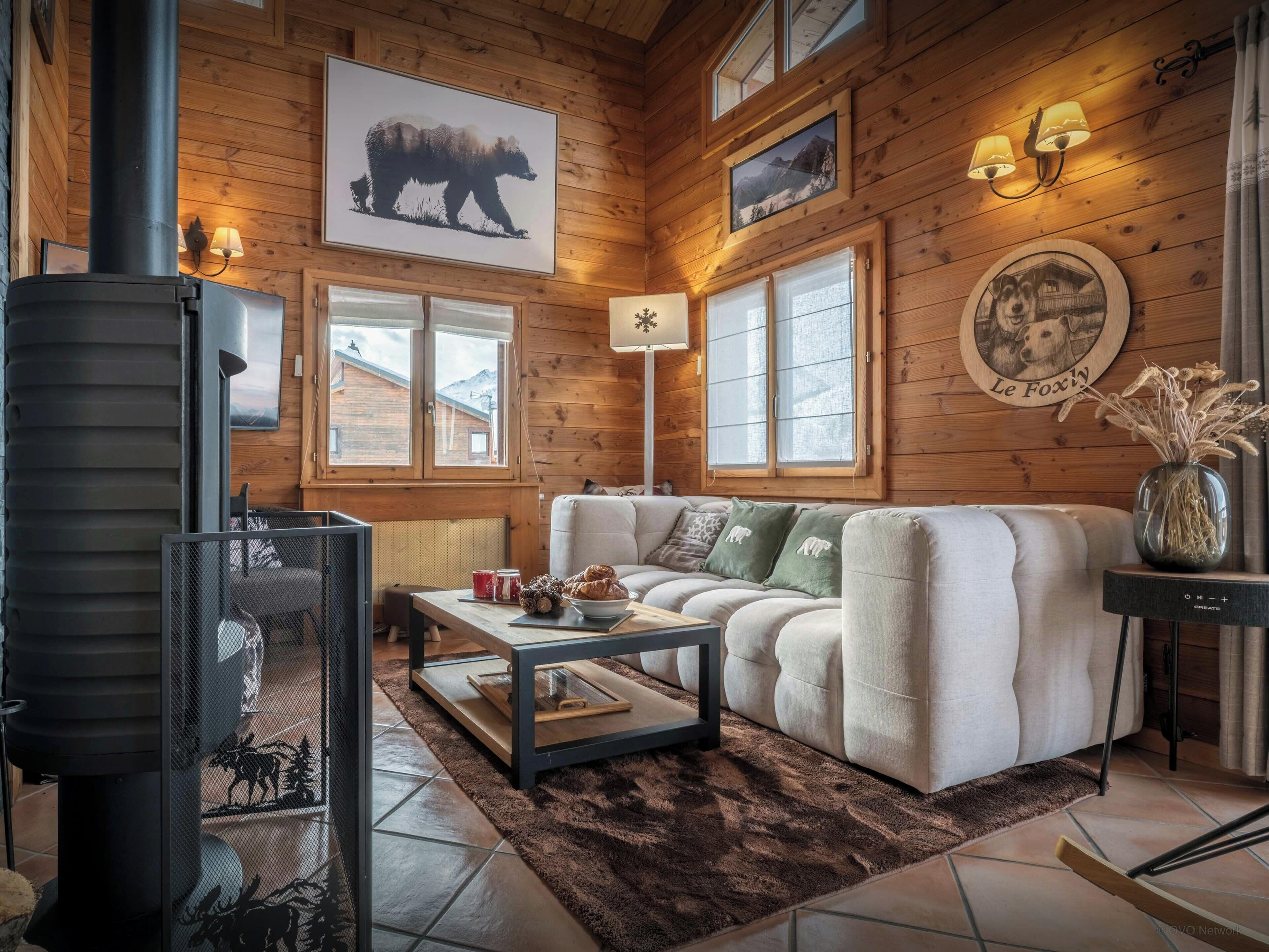 Un acogedor interior de cabaña de madera con chimenea, un conjunto de sofás y una mesa de comedor.