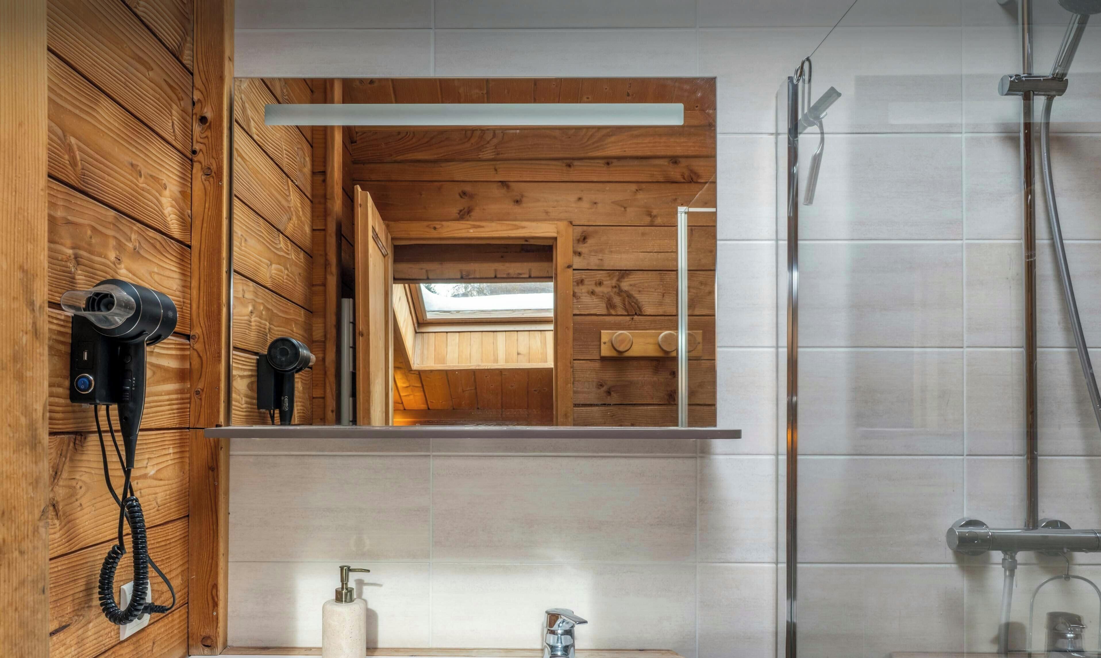 Ein Badezimmer mit Holzvertäfelung, einem Spiegel, einem Föhn, einem Waschbecken und einer Dusche.