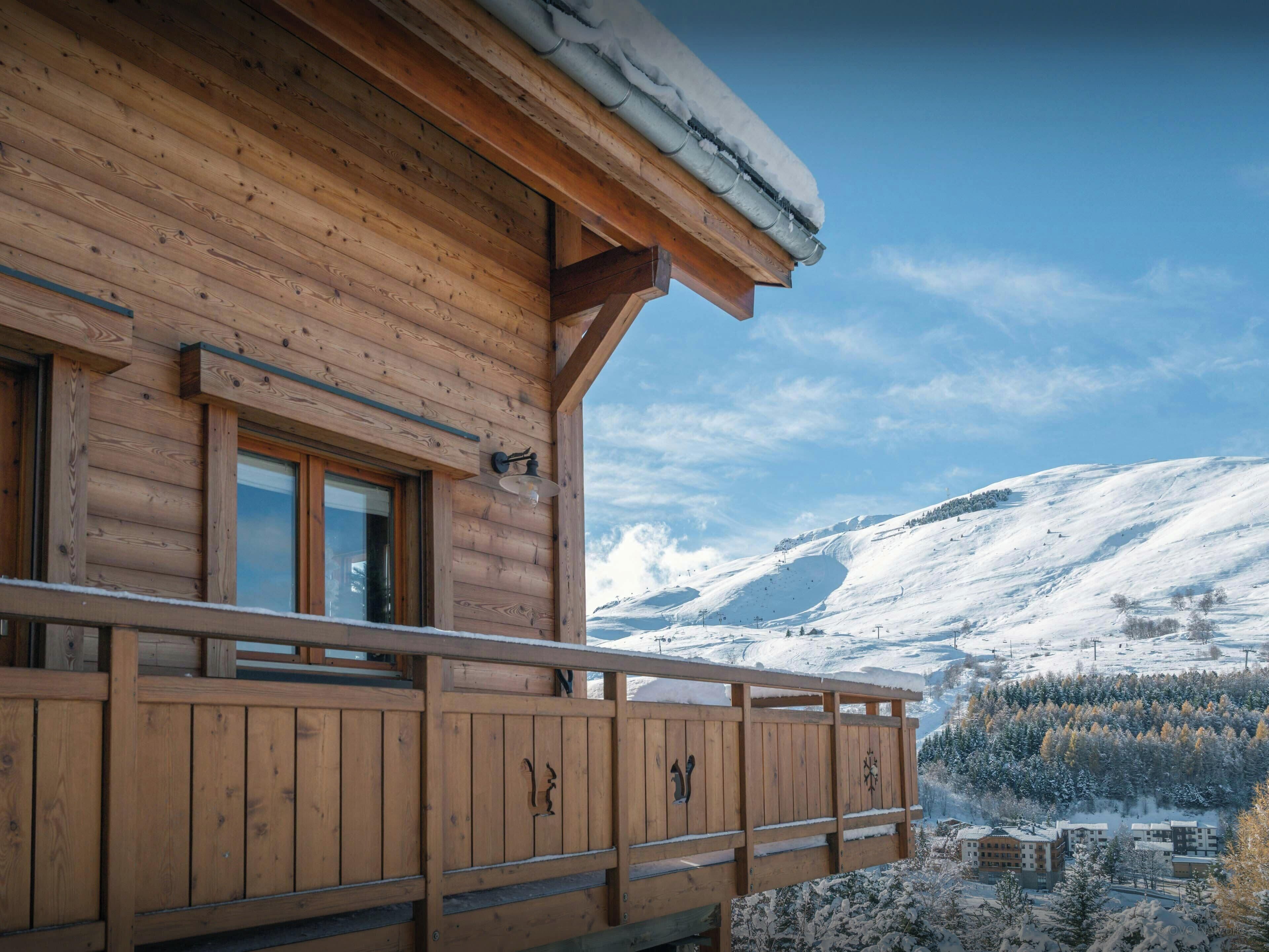 Une cabane en bois dotée d’un balcon donnant sur un paysage montagneux enneigé.