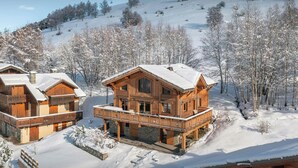 A wooden chalet with a balcony, surrounded by snow-covered trees and a ski slope in the background. - Chalet Foxly - Well-located, family-friendly chalet - OVO Network (Les Deux Alpes)