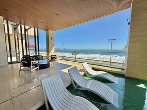 A modern indoor pool area with lounge chairs and a view of the beach. - The O apartments (Mazatlán)