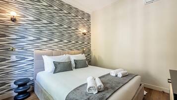 Ein modernes Hotelzimmer mit Wandpaneelen, einem Bett mit weißen Leinentüchern, zwei Kissen und einem Nachttisch mit Lampe.