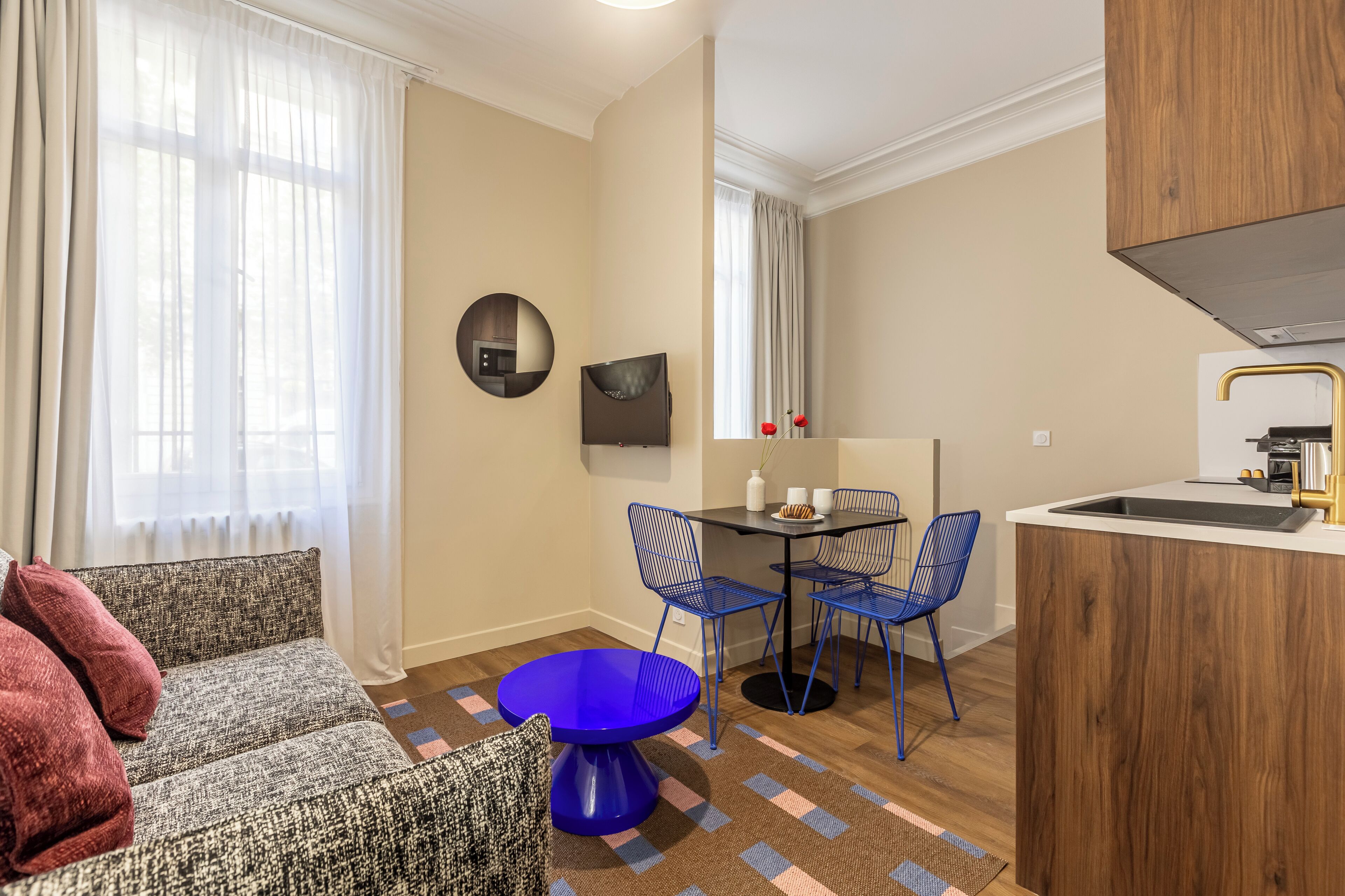 A compact living space with a sofa, a round blue table, and a kitchen area with a sink and a stove.